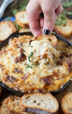 a person dipping cheese onto bread in a skillet with garlic and herbs on the side