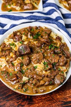 a bowl filled with meat and potatoes covered in gravy on top of a wooden table