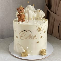 a white cake with gold stars and a teddy bear on top that says, one