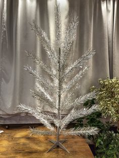 a silver christmas tree sitting on top of a wooden table next to a potted plant