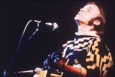 a man singing into a microphone while holding a guitar in his right hand and looking up at the sky