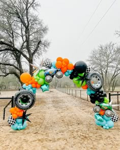 an arch made out of balloons in the shape of cars and racing wheels on dirt road