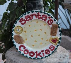 a plate that says santa's cookies on it sitting on a rock next to a potted plant