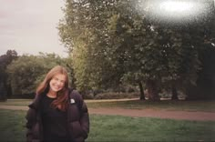 a woman is standing in the grass with trees behind her and smiling at the camera