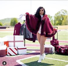 a woman in a fur coat and boots standing on a field next to suitcases