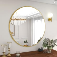 a round mirror on the wall above a table with candles and flowers in vases