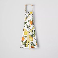 a white apron with oranges and lemons printed on it, tied to a wooden hanger