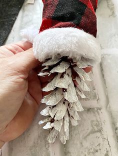 a hand holding a pine cone with snow flakes on it and wearing a santa hat