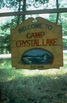 the welcome sign to camp crystal lake is hanging from a wooden fence in front of some trees