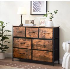 a wooden dresser with drawers next to a lamp and potted plant on the floor