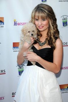 a woman holding a small dog in her hands on the red carpet at an event