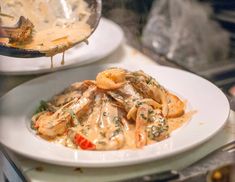 pasta with sauce and shrimp in a white bowl on a plate next to another dish