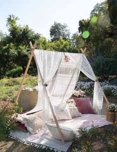 an outdoor bed with white sheets and pillows on it in the middle of some flowers