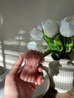 a person holding a piece of food next to a vase with white flowers in it