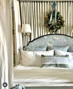 a bed with white sheets, pillows and a wreath hanging on the wall above it