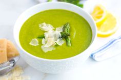 a bowl of green soup with asparagus, cheese and lemon slices on the side