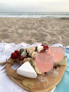 two glasses of wine, cheese and strawberries sit on a tray at the beach