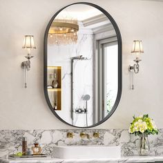 a bathroom with marble counter tops and a round mirror above the sink, along with two vases filled with flowers