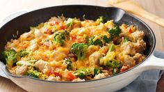 a skillet filled with chicken and vegetables on top of a wooden table next to utensils