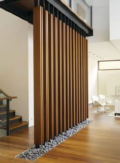 a wooden slatted wall next to a stair case in a living room with wood flooring