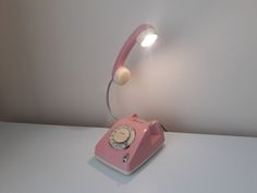 a pink phone with a light on top of it sitting on a white table next to a wall