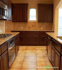 an empty kitchen with brown cabinets and marble counter tops, along with tile flooring