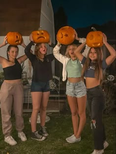 four girls holding pumpkins with faces drawn on them in front of a house at night