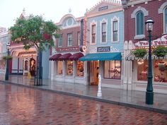 an empty street in front of several shops with umbrellas on the windows and people walking down the sidewalk