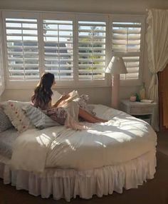 a woman sitting on top of a bed next to a window covered in white blinds