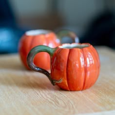 two orange pumpkin shaped mugs sitting on top of a wooden table next to each other