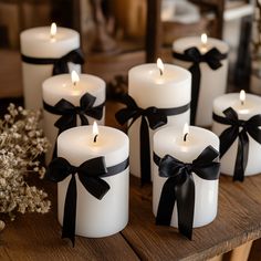 six white candles with black bows on them sitting on a wooden table next to flowers