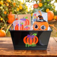 a black basket filled with halloween items on top of a wooden table next to pumpkins