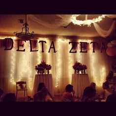 some people are sitting at tables with lights on the wall behind them and there is a sign that says delta zein