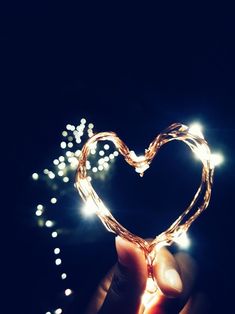 a hand holding a heart shaped object with string lights in the shape of a heart