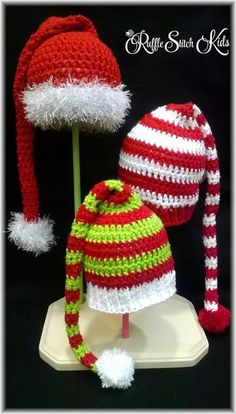 two crocheted hats and a hat on top of a white stand with red and green stripes