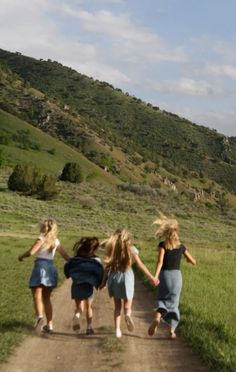 four girls walking down a dirt road holding hands in the middle of an open field