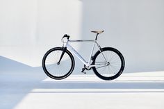 a bike parked in front of a white wall with the sun shining on it's rims