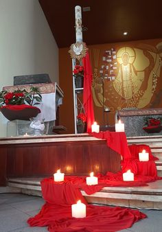 candles are lit in front of the alter at a church with red cloth draped around it