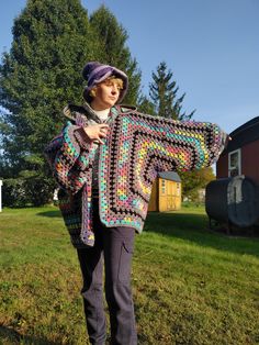 a woman standing in the grass holding up a crocheted granny's shawl