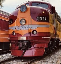 an orange and red train is on the tracks next to another yellow train in the background