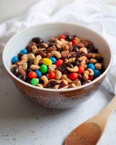 a bowl filled with cereal and m & m's next to a wooden spoon