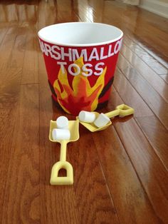 a cup with marshmallows on the floor next to a pair of tongs