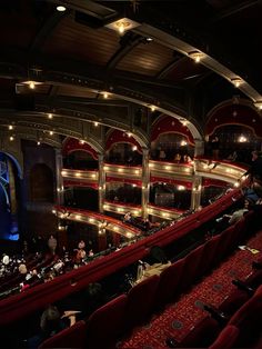 an auditorium filled with people sitting on red seats and looking at the stage from above