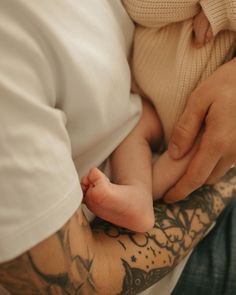 a man holding a baby in his arms with tattoos on it's arm and chest