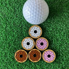 six donuts are placed next to a golf ball on the green grass with holes in it