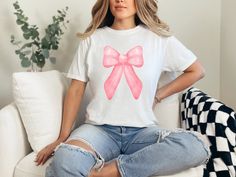 Indulge in the perfect gift for Mom with a trendy coquette pink bow aesthetic on her birthday or for Mother's Day - our Comfort Colors T-shirts.  Crafted from the finest 100% ring-spun USA cotton, these shirts offer unmatched comfort with a medium weight, pre-shrunk fabric.  Our ethically grown and harvested cotton ensures not just a soft touch but also a clear conscience.  The garment-dyed, soft-washed fabric brings an extra layer of coziness to their wardrobe, making these tees an ideal daily choice.  The relaxed fit offers both style and comfort, while the double-needle stitching ensures durability that stands the test of time.  Say goodbye to side-seams as our tubular-shaped shirts maintain their form effortlessly.  Elevate gifting with the perfect blend of quality, style, and personal Cute Pink T-shirt With Bow, Trendy Pink Tops For Birthday, Trendy Pink T-shirt For Birthday, Pink Tops With Bow For Party, Pink Party Top With Bow, Cute Party Tops With Bow, Cute Party Tops With Bow Detail, Pink T-shirt With Bow For Summer, Pink Crew Neck T-shirt With Bow