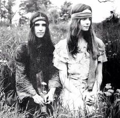 two women sitting in tall grass with long hair and head scarves on their heads