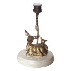 a brass deer and calf figurine sitting on a marble base with a light fixture in the background