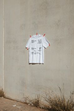 a white t - shirt hanging on the side of a building with red pins attached to it