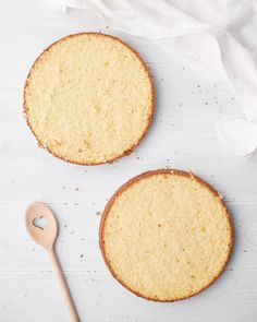 two cakes sitting on top of a white table next to a wooden spoon and napkin